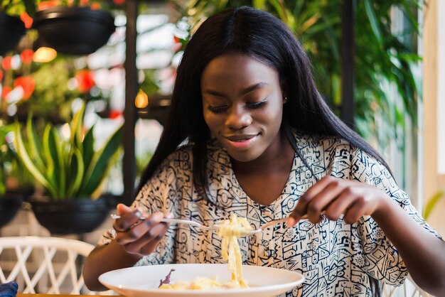 Joven africana comiendo espaguetis en restaurante.