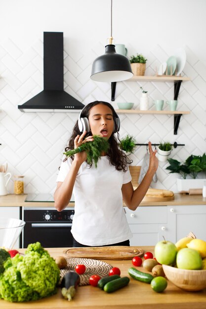 Joven africana emocional está escuchando música a través de auriculares y cantando tiene eneldo