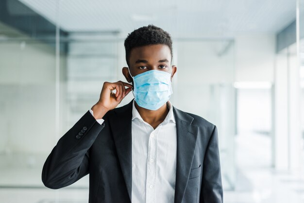 Joven africana en máscara médica en su rostro en la oficina