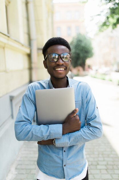 Joven africana de pie celebrando el éxito en la calle mirando su computadora portátil en la mano