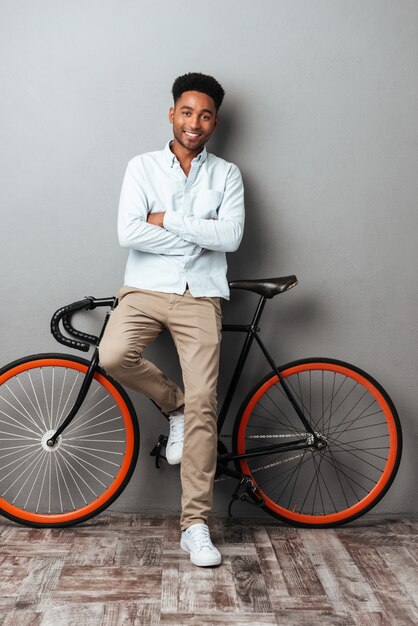 Joven africana de pie sobre la pared gris con bicicleta.