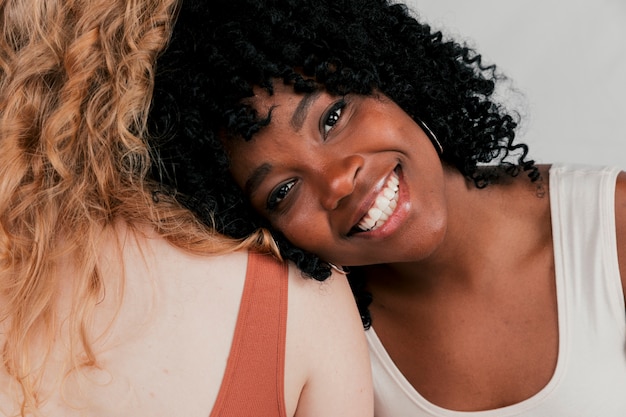 Una joven africana sonriente apoyada en el hombro de su amiga con piel blanca