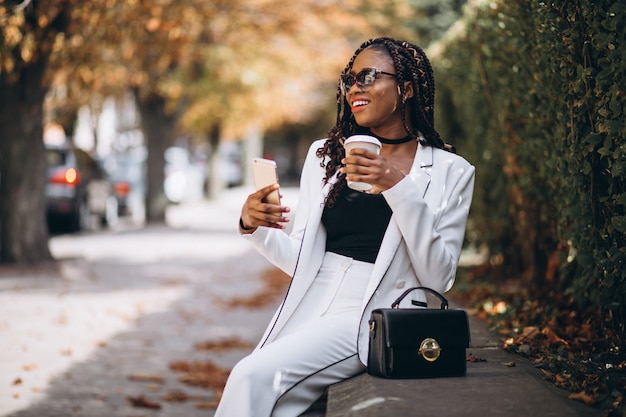 Joven africana tomando café y usando el teléfono