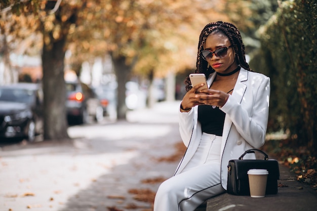 Joven africana tomando café y usando el teléfono