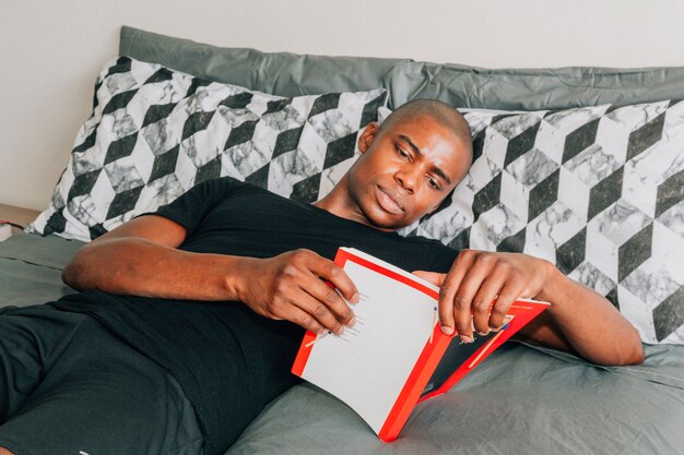 Un joven africano acostado en la cama leyendo el libro