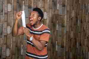 Foto gratuita joven africano que se siente emocionado y feliz mientras sostiene una hoja de papel y le grita con alegría