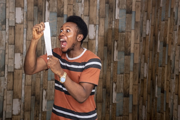 Joven africano que se siente emocionado y feliz mientras sostiene una hoja de papel y le grita con alegría