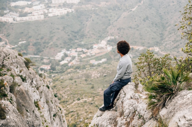 Un joven africano sentado en una roca con vistas a la montaña