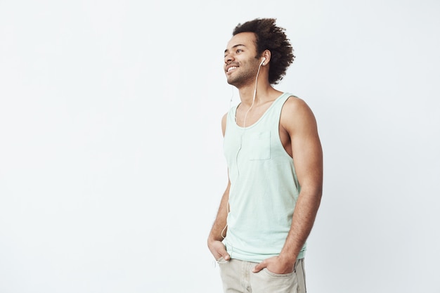 Joven africano sonriendo escuchando música alegre en streaming con auriculares con cable esperando un buen ritmo para comenzar a bailar mirando a la izquierda.