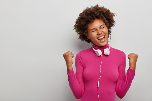 Joven afroamericana aclama el éxito, se encuentra en pose triunfante feliz en el estudio