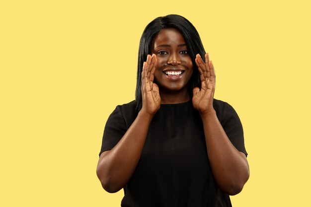 Joven afroamericana aislada en espacio amarillo, expresión facial. Hermoso retrato femenino de medio cuerpo.