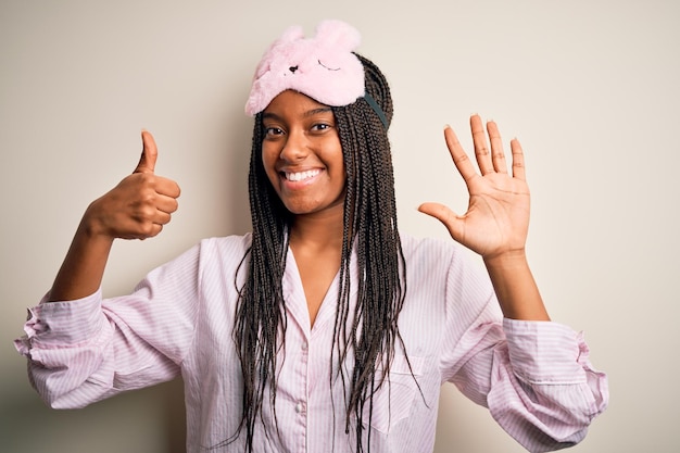 Foto gratuita joven afroamericana con pijama rosa y máscara para dormir sobre un fondo aislado que aparece y señala con los dedos número seis mientras sonríe confiada y feliz