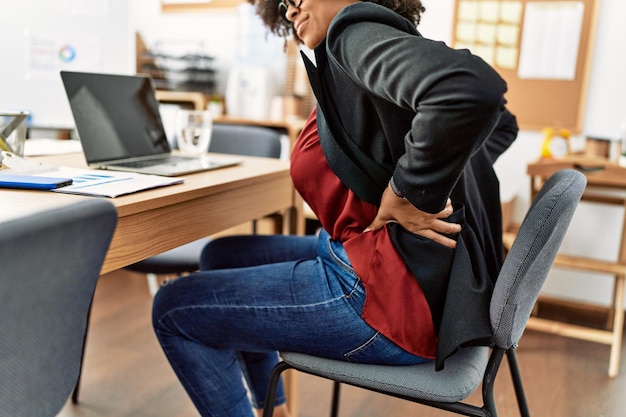 Joven afroamericana que sufre de dolor de espalda trabajando en la oficina