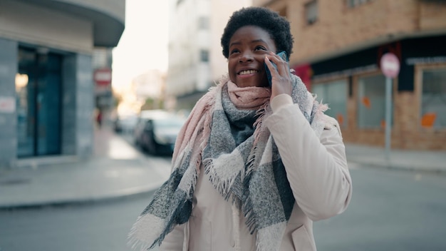 Joven afroamericana sonriendo confiada hablando por el teléfono inteligente en la calle