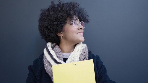 Joven afroamericana sonriendo confiada sosteniendo una carpeta sobre un fondo negro aislado