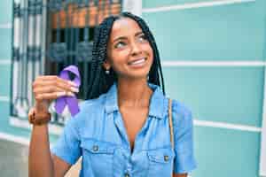 Foto gratuita joven afroamericana sonriendo feliz sosteniendo una cinta morada caminando en la ciudad
