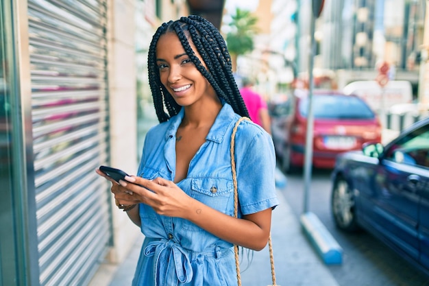 Joven afroamericana sonriendo feliz usando un teléfono inteligente en la ciudad.