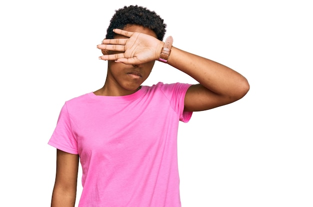 Joven afroamericana vestida con ropa informal que cubre los ojos con el brazo con aspecto serio y triste de escondite ciego y concepto de rechazo