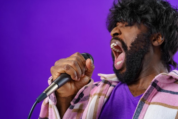 Joven afroamericano barbudo cantando en el micrófono contra el fondo púrpura