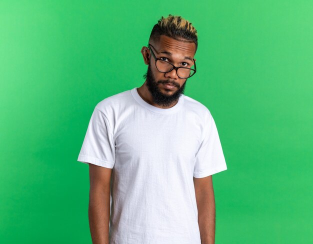 Joven afroamericano en camiseta blanca con gafas mirando a cámara desconcertado