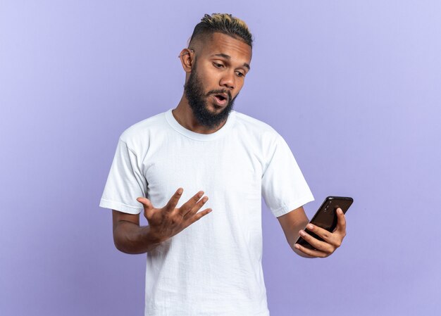 Joven afroamericano en camiseta blanca mirando la pantalla de su teléfono inteligente