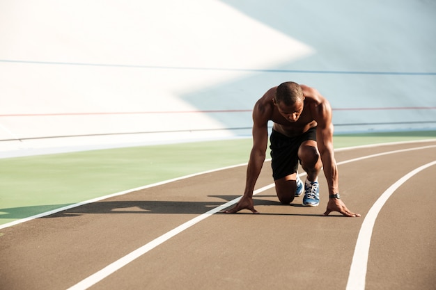 Joven afroamericano deportista en posición inicial listo para comenzar en la pista deportiva en el estadio