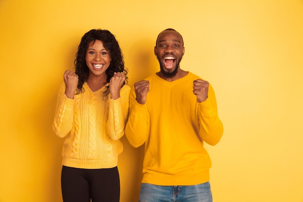 Joven afroamericano emocional y mujer en ropa casual brillante posando sobre fondo amarillo. Hermosa pareja. Concepto de emociones humanas, expresión facial, relaciones, anuncio. Feliz celebración.