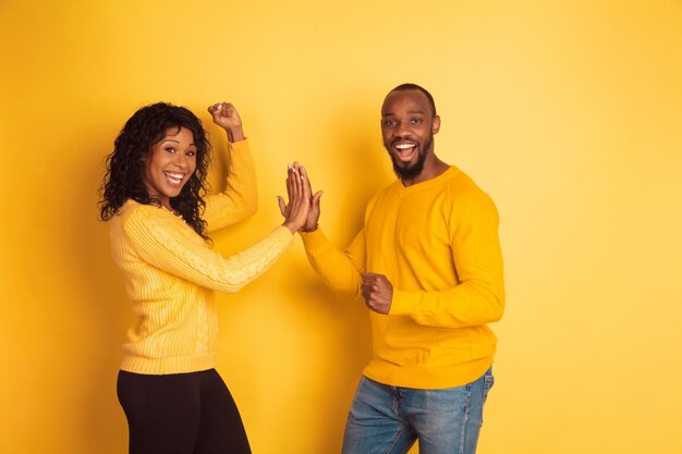 Joven afroamericano emocional y mujer en ropa casual brillante posando sobre fondo amarillo. Hermosa pareja. Concepto de emociones humanas, expresión facial, relaciones, anuncio. Trabajo en equipo.