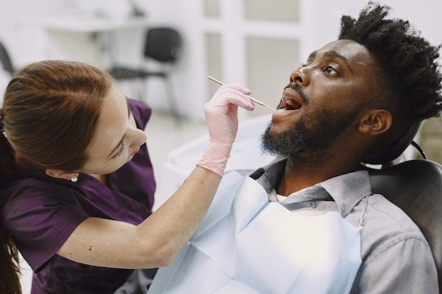 Joven afroamericano. Guy visitando el consultorio del dentista para la prevención de la cavidad bucal. Médico hombre y mujer mientras chequeo de dientes.
