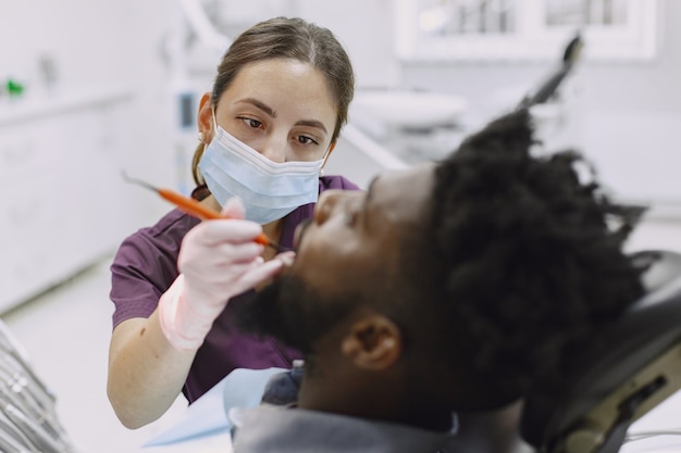 Joven afroamericano. Guy visitando el consultorio del dentista para la prevención de la cavidad bucal. Médico hombre y mujer mientras chequeo de dientes.