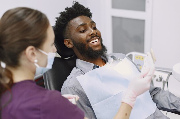 Joven afroamericano. Guy visitando el consultorio del dentista para la prevención de la cavidad bucal. Médico hombre y mujer mientras chequeo de dientes.