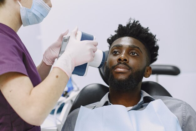 Joven afroamericano. Guy visitando el consultorio del dentista para la prevención de la cavidad bucal. Médico hombre y mujer mientras chequeo de dientes.