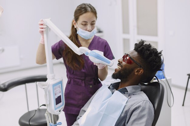 Joven afroamericano. Guy visitando el consultorio del dentista para la prevención de la cavidad bucal. Médico hombre y mujer mientras chequeo de dientes.