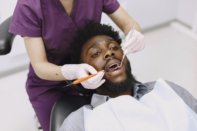 Joven afroamericano. Guy visitando el consultorio del dentista para la prevención de la cavidad bucal. Médico hombre y mujer mientras chequeo de dientes.