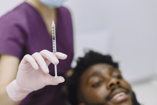 Joven afroamericano. Guy visitando el consultorio del dentista para la prevención de la cavidad bucal. Médico hombre y mujer mientras chequeo de dientes.