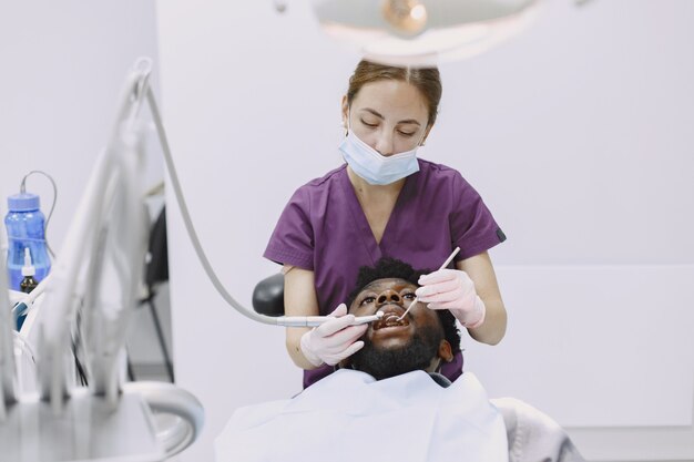 Joven afroamericano. Guy visitando el consultorio del dentista para la prevención de la cavidad bucal. Médico hombre y mujer mientras chequeo de dientes.