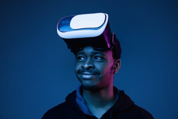 Joven afroamericano jugando con gafas VR en luz de neón en gradiente.