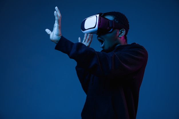 Joven afroamericano jugando con gafas VR en luz de neón en gradiente.