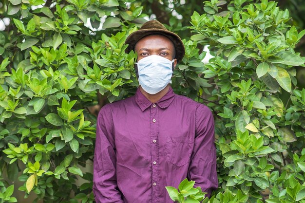 Joven afroamericano en una mascarilla protectora de pie en un arbusto