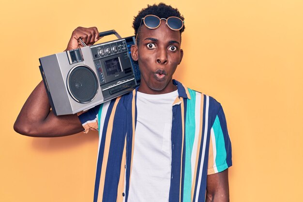 Joven afroamericano sosteniendo boombox escuchando música asustado y asombrado con la boca abierta por la cara de incredulidad sorpresa