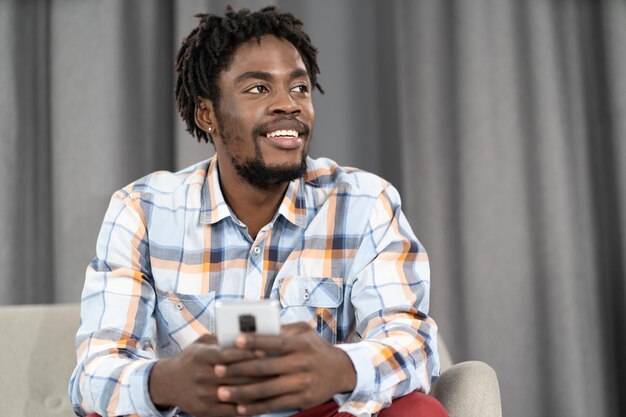 Joven afroamericano sosteniendo un teléfono inteligente en la mano mirando hacia otro lado