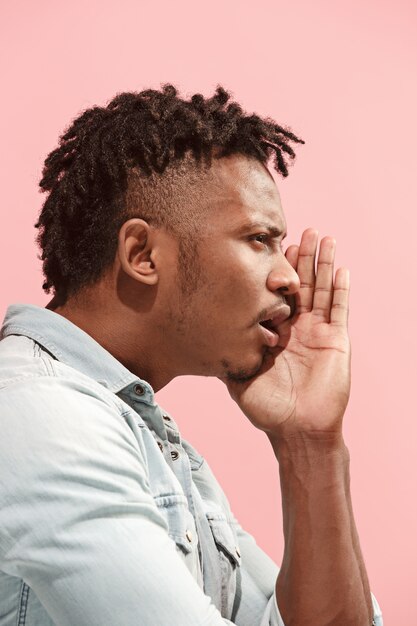 El joven afroamericano susurrando un secreto detrás de su mano sobre la pared rosa