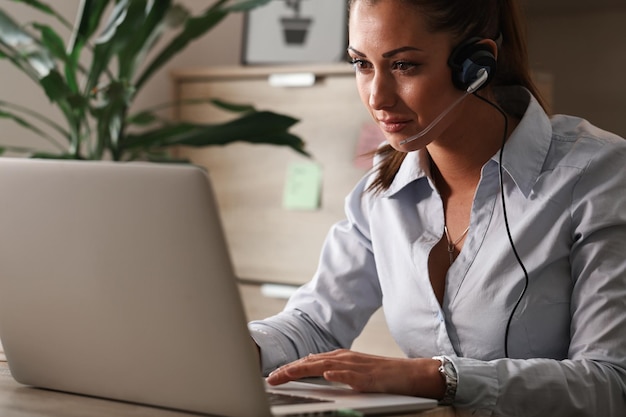 Joven agente de atención al cliente con auriculares trabajando en una computadora portátil en un centro de llamadas