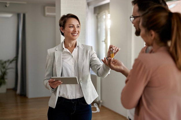 Joven agente inmobiliario feliz dando llaves de casa a una pareja que está comprando una casa nueva