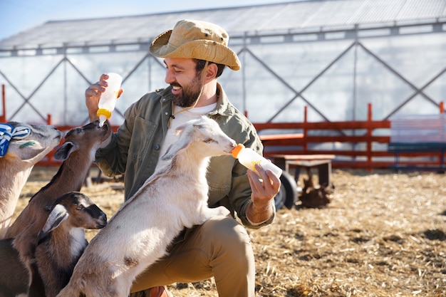 Joven agricultor alimentando a sus cabras con leche de una botella en la granja