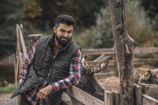 Foto gratuita joven agricultor de pelo oscuro de pie cerca del corral de ganado