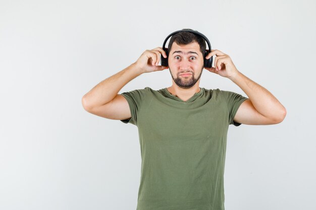 Joven ajustando auriculares en camiseta verde y mirando perplejo