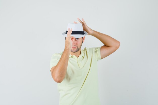 Joven ajustando su sombrero en camiseta y mirando confiado