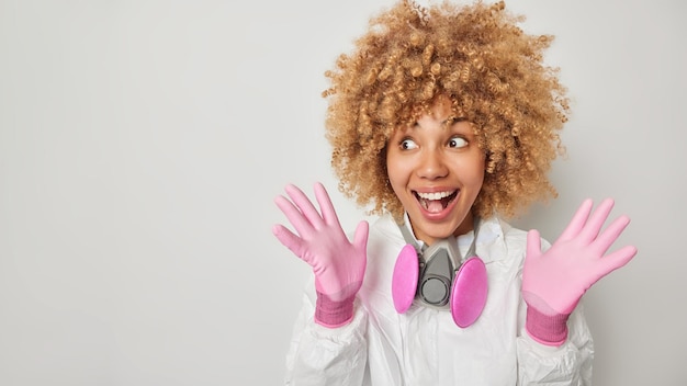 Foto gratuita una joven alegre e impresionada se ve alegremente a un lado y usa un traje protector de materiales peligrosos y un respirador de guantes alrededor del cuello vestidos para la protección contra el coronavirus aislado sobre un espacio en blanco de fondo gris