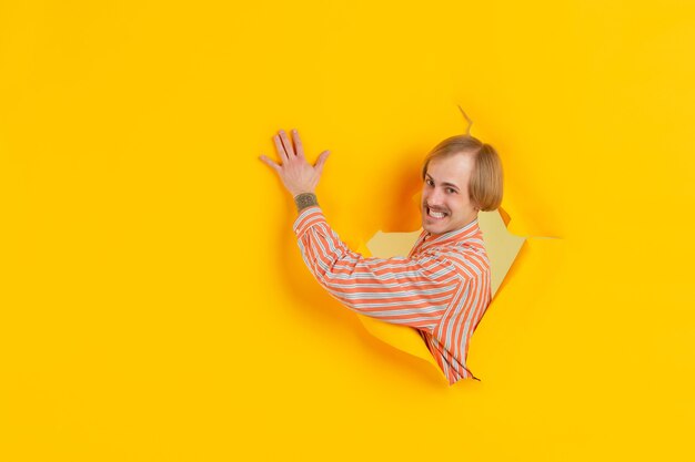Joven alegre posa en pared de agujero de papel amarillo rasgado emocional y expresivo